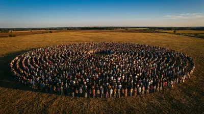 A vast gathering of people standing together in an open field at golden hour, forming a wide circular pattern